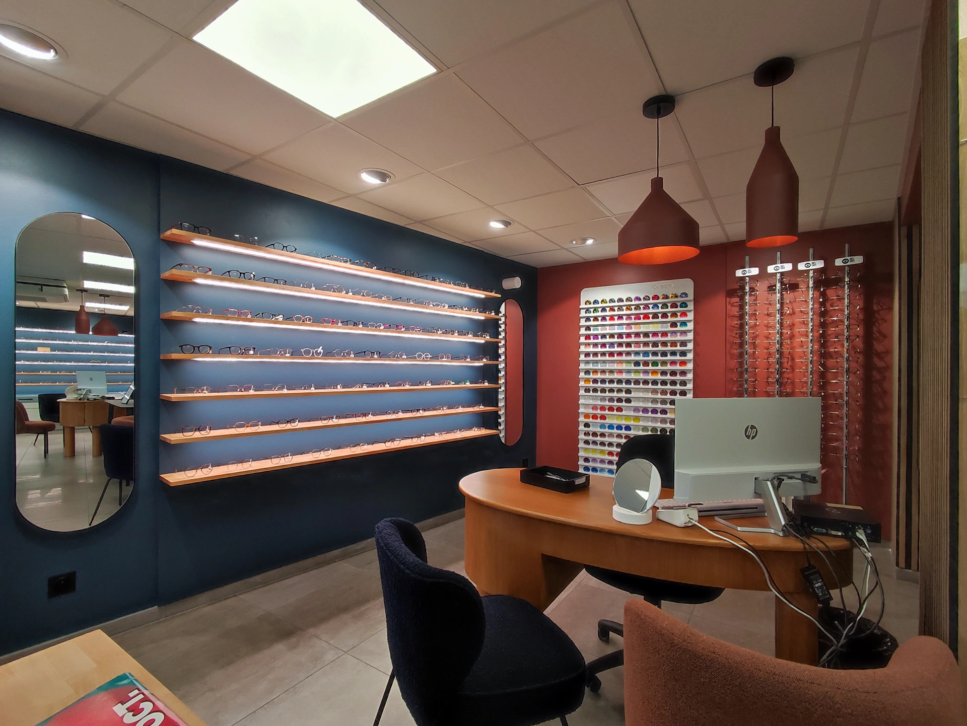 Espace d'attente moderne dans la boutique professionnelle d'Hadecoville, des lampes suspendues contemporaines, des murs bleus et rouges et des étagères en bois encastrées - un mélange parfait de style contemporain et de confort accueillant.